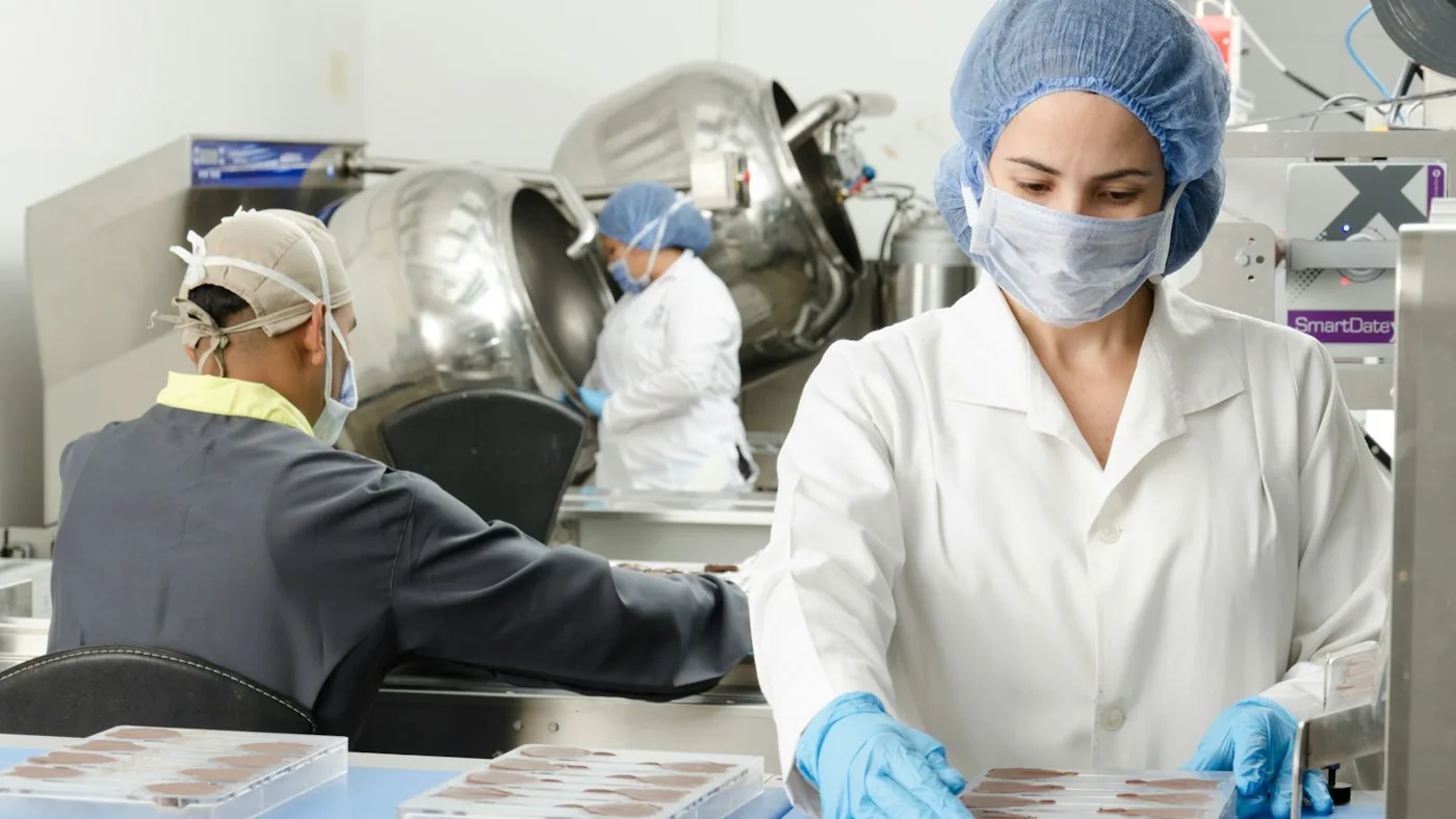 Equipe com touca e jaleco na linha de produção de alimentos
